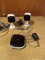 Two Panasonic home security cameras with stands, a black and white Panasonic base station, and power adapters on a wooden surface