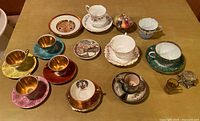 Photo showing a variety of vintage teacups with gold interiors along with matching saucers and decorative plates spread on a table.