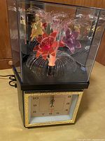 Full view of the vintage fiber optic flower clock, showing the front clock face, flower arrangement with fiber optic strands, and protective enclosure.