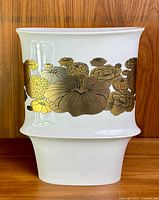 Front view of white cylindrical vase with gold and silver floral pattern around center.
