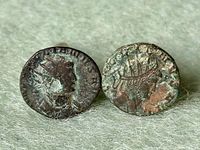 Pair of ancient Roman bronze coins mounted as cufflinks resting on fabric, showing obverse and reverse sides.
