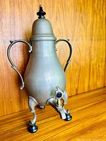 Front view of antique pewter coffee samovar showing footed base, handles, lid with finial, and front spigot