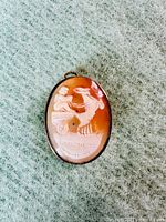 Front view of the oval shell cameo with a carved classical chariot scene set in a silver frame.