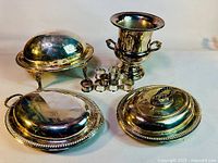 Several silver plated serving pieces including covered server, chafing dishes, champagne bucket and napkin rings shown on a beige surface
