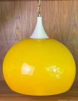 Yellow plexiglass pendant lamp showing the rounded globe shade and the white metal fitting on top, with chain mount.
