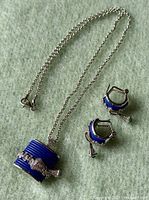Photo shows the necklace and earrings set against a soft green background, highlighting blue enamel and sapphire stones.