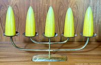Front view of the brass candelabra with all five yellow taper candles installed, showing the design and candle shape.