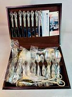 Full set of Rogers Bros silverplated flatware displayed inside original box, showing knives in slots on lid and various forks, spoons, serving pieces in the base, many in original plastic sleeves.