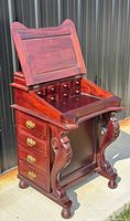 Fashioned Victorian style mahogany Davenport desk shown closed with carved side supports and brass handles on drawers.