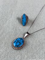 Both turquoise sterling silver ring and pendant necklace shown on fabric background.