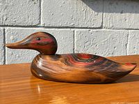 Side view of the vintage wooden carved duck showing wood grain and painted red accents on the head and body.
