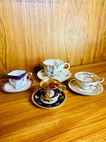 Four vintage demitasse cups and saucers against a wooden background, showing their designs and condition