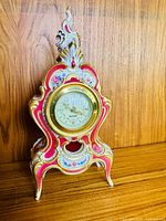 Porcelain Rococo mantel clock with ornate hand-painted floral designs on wooden surface background.