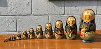Full set of 12 dolls in descending size order on wooden surface against brick wall