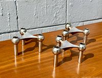 Set of three chrome modular tripod candle holders displayed on wood surface, showing geometric design and spherical sockets