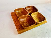 Front and angled view showing four solid teak square serving bowls arranged on a rectangular teak tray with handle.