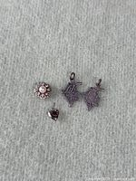 Array of four silver pendants displayed on fabric background including heart, flower, and maple leaf designs.