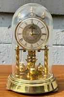 Front view of vintage Solar mantel clock under domed glass, showing decorative dial with Roman numerals and four-sphere pendulum.
