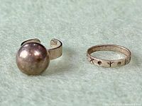 Photo of both vintage modernist rings on a soft surface, showing the statement ball ring and the elements band ring with stamped motifs.