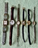 Top-down photo showing seven vintage ladies watches arranged side by side with various band materials and face shapes.