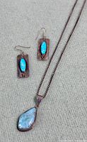 Photo of the Larimar pendant necklace and earrings laid flat on grey fabric showing color and style details.
