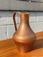 Side view of hand-hammered copper pitcher showing hammered texture and curved handle.