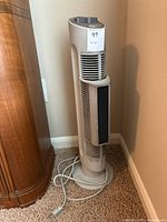 Full view of Sharper Image 26-inch tower air purifier with power cord coiled at base, positioned next to wooden furniture near wall.