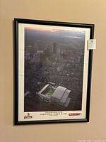 Framed photo showing aerial view of Houston with Enron Field stadium during inaugural Astros game, reflections on glass visible.