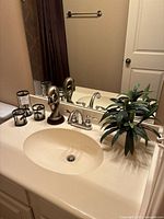 Candleholders, resin sculpture, and artificial plant arranged on bathroom sink counter in front of mirror
