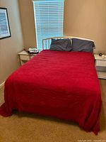 Front view of white wooden bed frame with red bedspread and gray pillows in a bedroom setting.