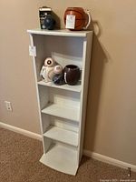 Front view of tall, narrow white wooden bookcase with various sports-themed ball decorations on some shelves.