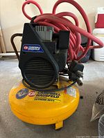 Front view of yellow pancake air compressor tank with the Campbell Hausfeld brand label and red air hose coiled on top.