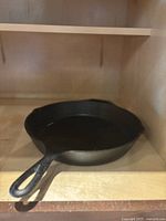 Side view of the cast iron skillet placed inside a cabinet shelf, showing the handle and skillet body.