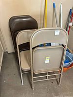 Four metal folding chairs, two beige and two brown, stacked and shown from front and back angles