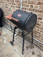 Full view of Char-Griller black barrel-style grill with wooden side shelf and metal stand with wheels.