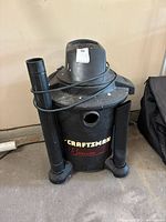 Front view of Craftsman 8-gallon wet/dry vacuum showing hose attachments and power cord on top, some dust and wear visible.