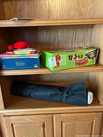 Shelf containing colorful board games, a Jumbo puzzle roll-up box, and a black fabric roll containing colored pencils.