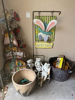 Full view of rustic garden and yard decor items including metal Easter bunny sign, frog figurines, metal bucket with wood pieces, garden stake with ladybugs and welcome sign.