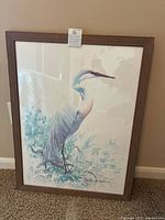 Framed watercolor serigraph of a heron, showing full image with artist signature visible, in a wooden frame against a wall.