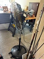 Side view of black HICFM pedestal fan, showing mesh grille, fan blades, adjustable pole, and wheeled base.