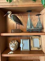 Wooden pelican and metal sailboat candleholder on upper shelf; ceramic shell bowl and two picture frames on lower shelf.