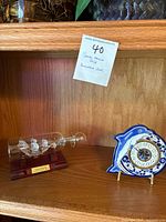 Photo of wooden shelf with blue and white hand painted ceramic ship clock and glass ship in bottle model with Santa Maria label.