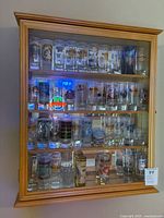Full view of wooden cabinet containing collection of branded shot glasses on four shelves.