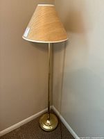 Full view of the brass-tone floor lamp standing in a corner with beige wall and carpeted floor.
