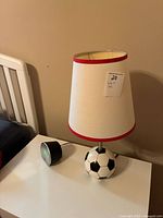 19-inch soccer ball base lamp with white lampshade with red trim, next to a black digital alarm clock