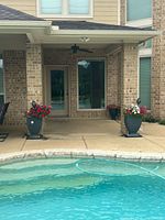 Two large dark gray outdoor planters placed on a patio beside pool area with live pink and white flowers inside.
