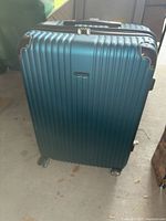 Front view of the teal blue Traveler's Choice rolling luggage showing the ribbed hard shell, metal corner protectors and spinner wheels.