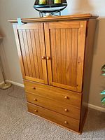 Front view of wooden media center cabinet showing two paneled doors and three drawers with minor scratches.