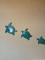 Three turquoise metal sea turtle wall sculptures of 6, 7, and 9 inch sizes, each with embossed sea turtle patterns, mounted on wall.