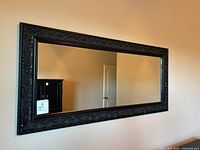 Straight-on view of ornate black framed rectangular mirror hanging on wall.